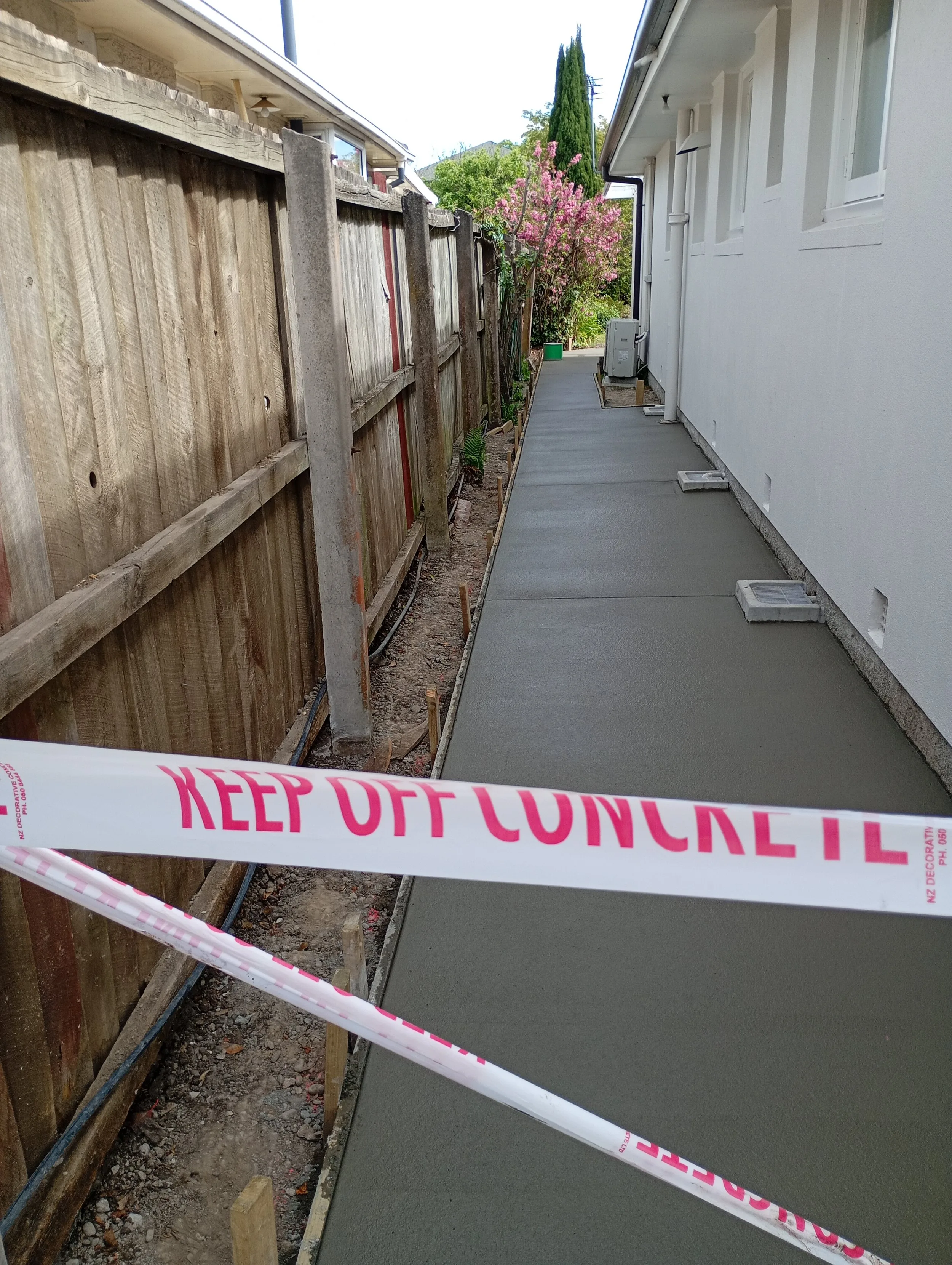 Freshly poured concrete path beside a house, taped off to cure